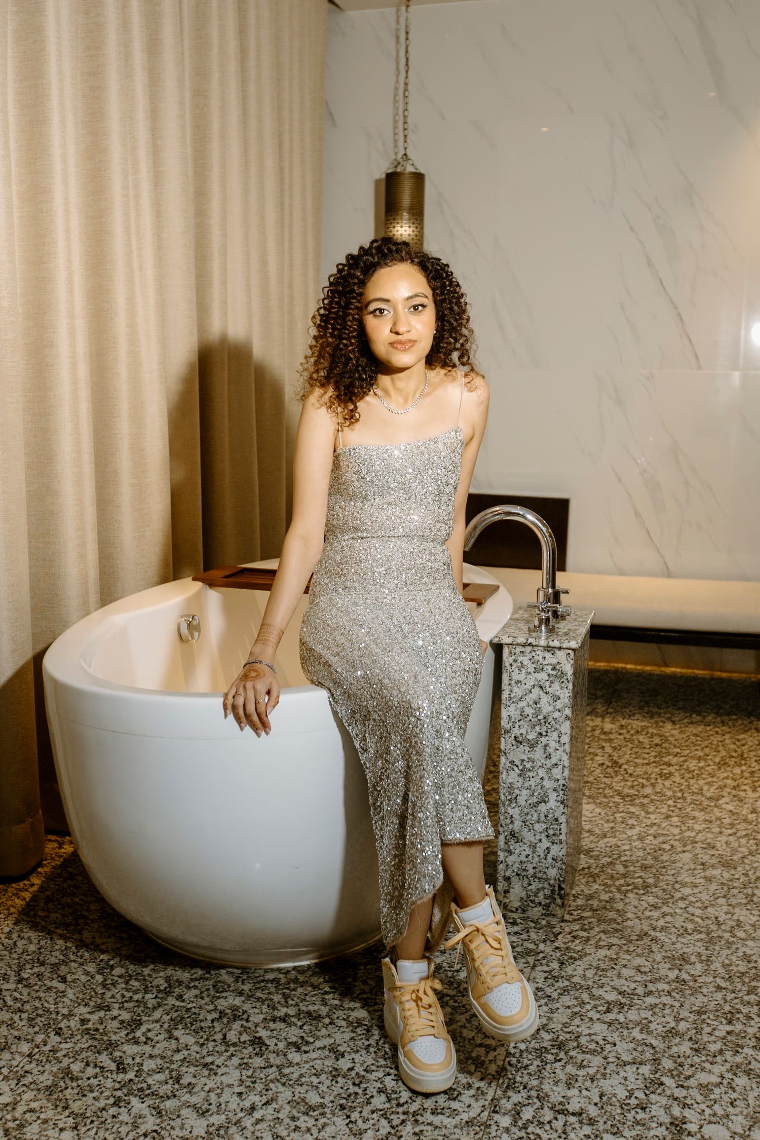 Sparkly silver dress photoshoot with modern bathtub and marble wall backdrop.