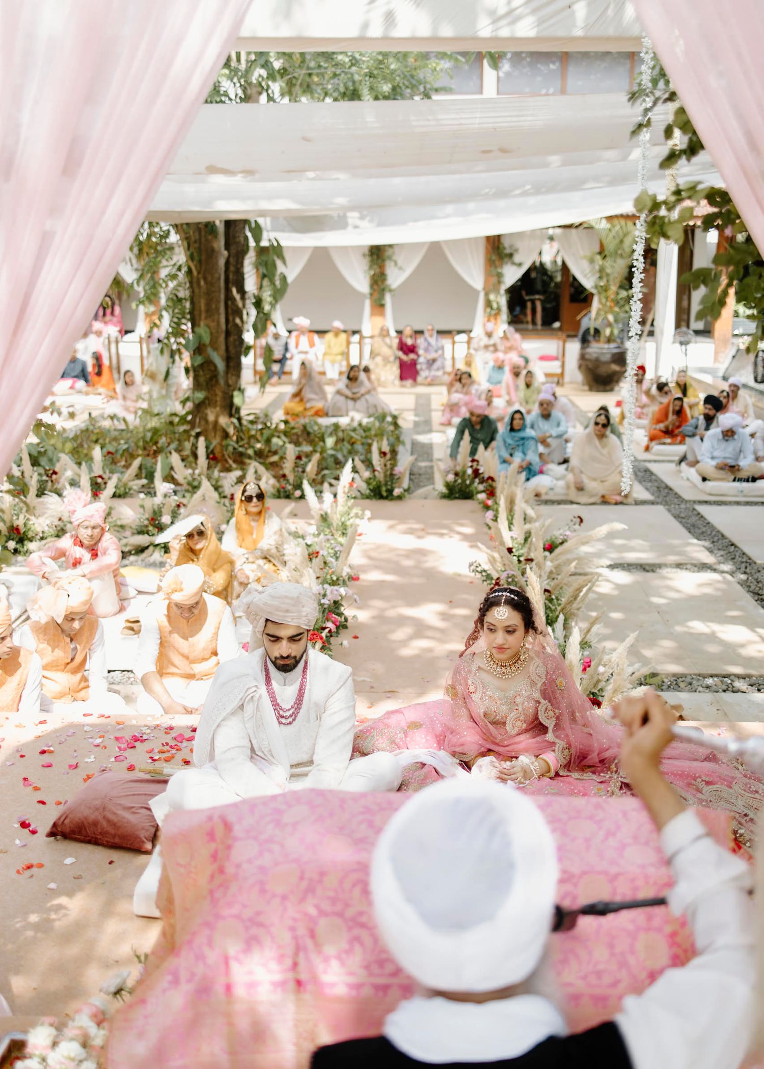 Traditional Indian wedding ceremony with guests seated on floor cushions under white canopy decorations.