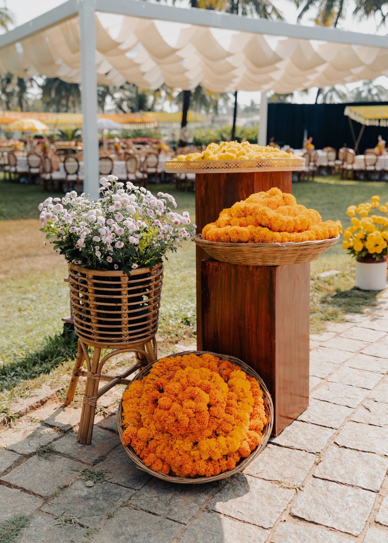 Vibrant orange marigold garlands and white flowers decorate an outdoor wedding setup with a canopy and wooden chairs.