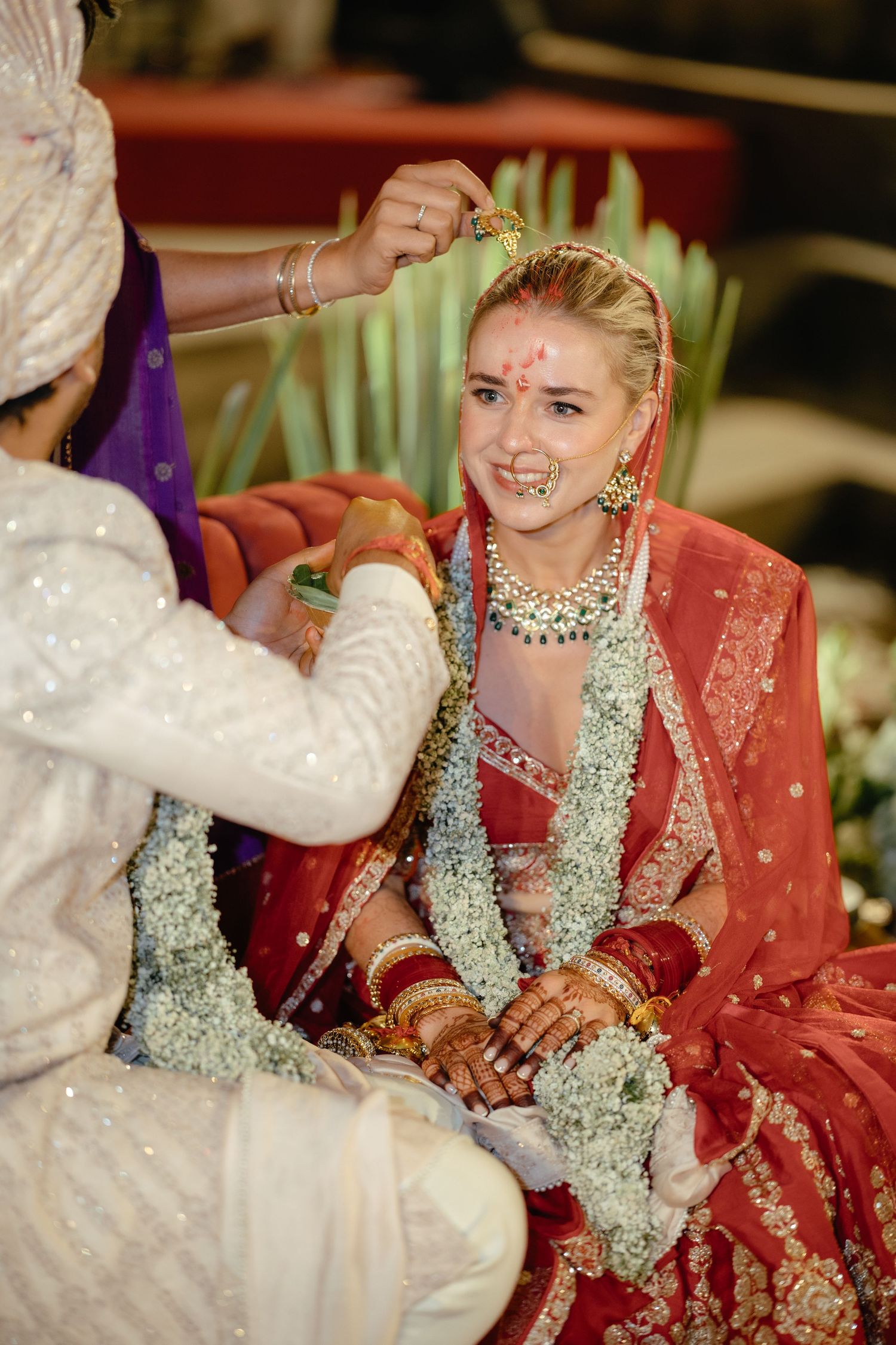 Wedding ceremony with bride in red and silver lehenga receiving traditional blessings.