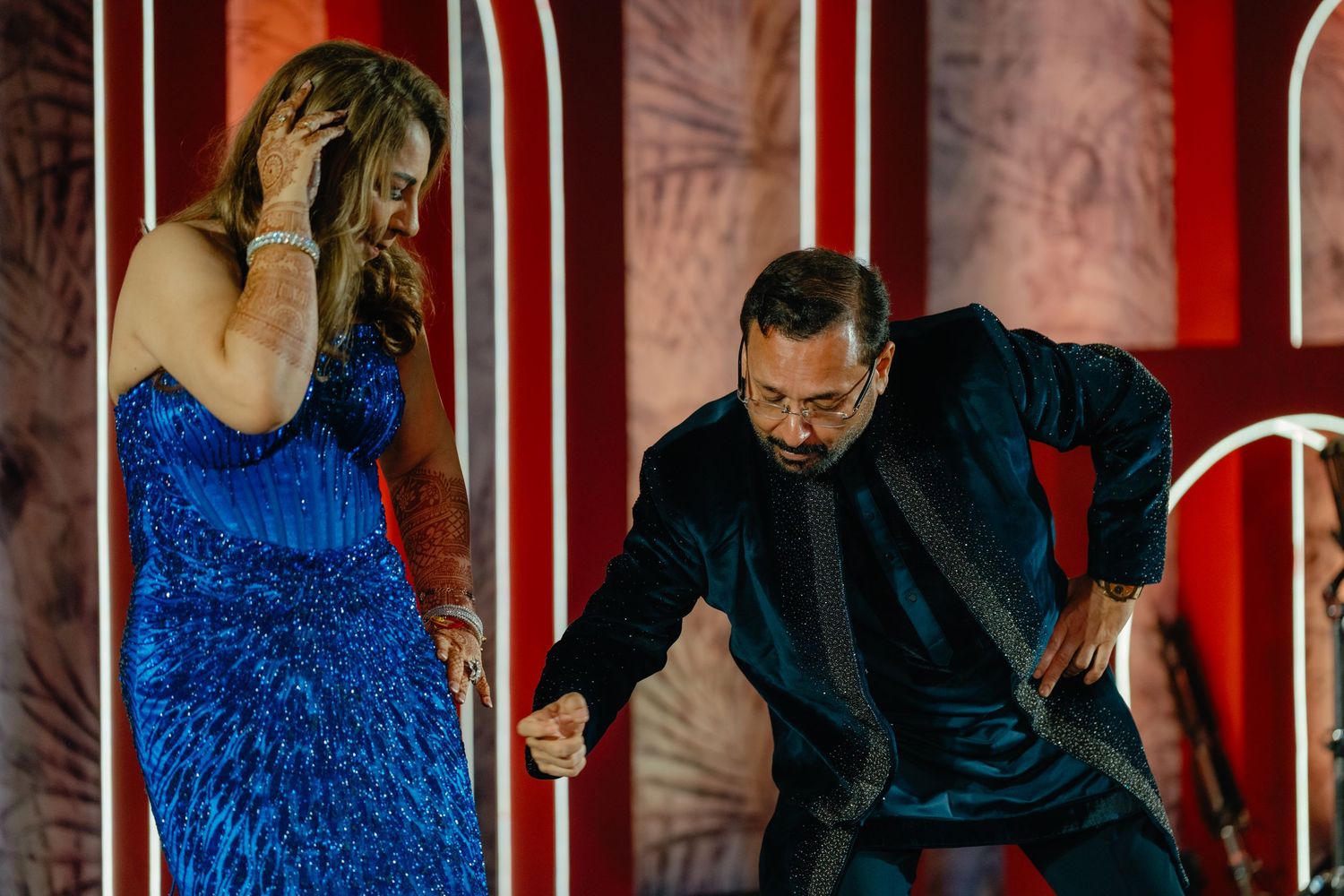 Two performers on stage during a show, with one wearing a sparkly blue dress and another in dark attire dancing.