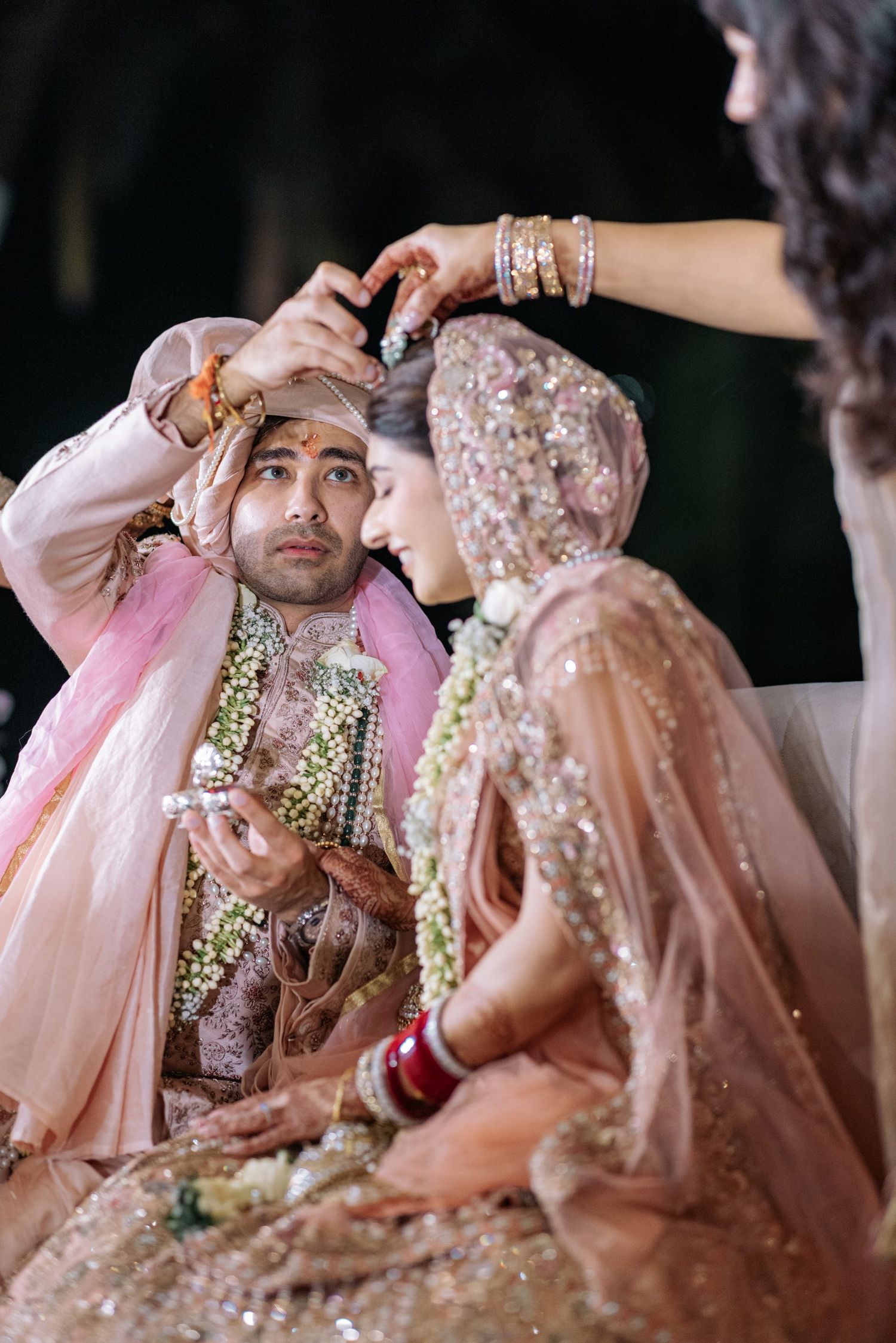 Close-up of traditional Indian wedding ritual showing detailed embroidered outfits and jewelry.