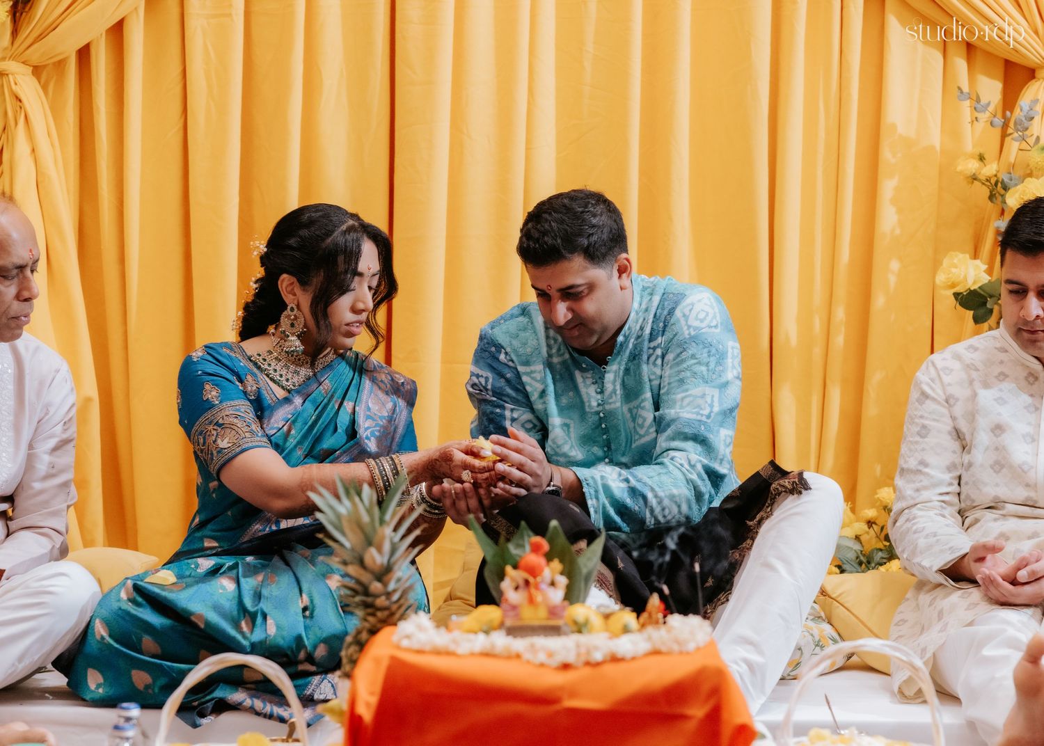 Bride and groom perform traditional Indian wedding ceremony ritual, exchanging offerings while seated on decorated mandap.