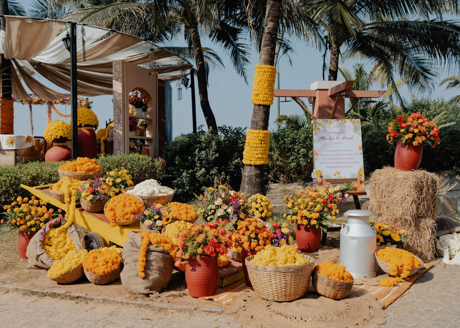 Tropical fruit stand display with colorful produce, hay bales, and palm trees along a beachfront location.