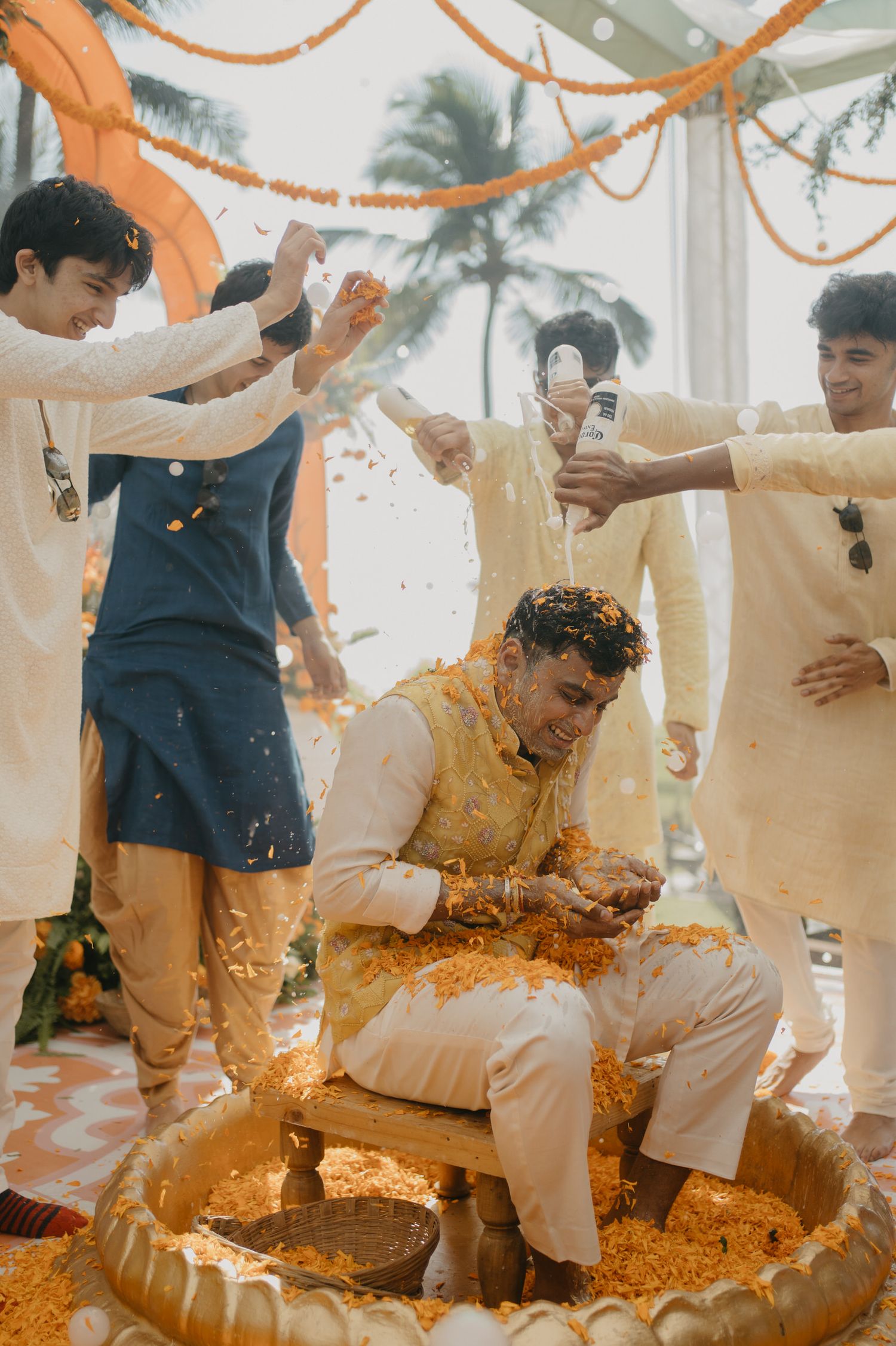 Traditional Indian Haldi ceremony celebration with turmeric paste being applied during a wedding ritual under orange decorations.