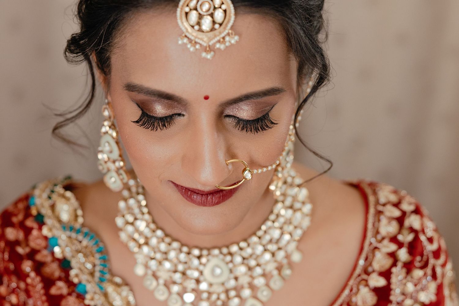 Traditional Indian bridal makeup and jewelry featuring pearl necklace, maang tikka and burgundy red lipstick.