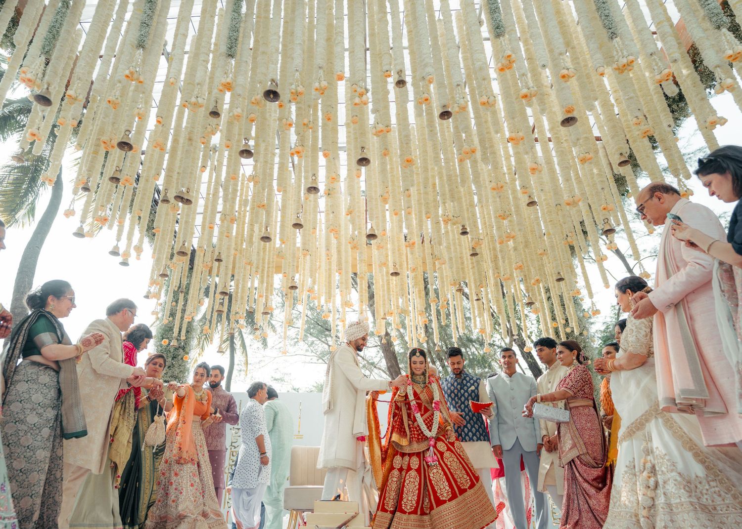 Elegant Indian wedding ceremony under a decorative canopy of hanging fabric and flowers in soft beige and orange tones.