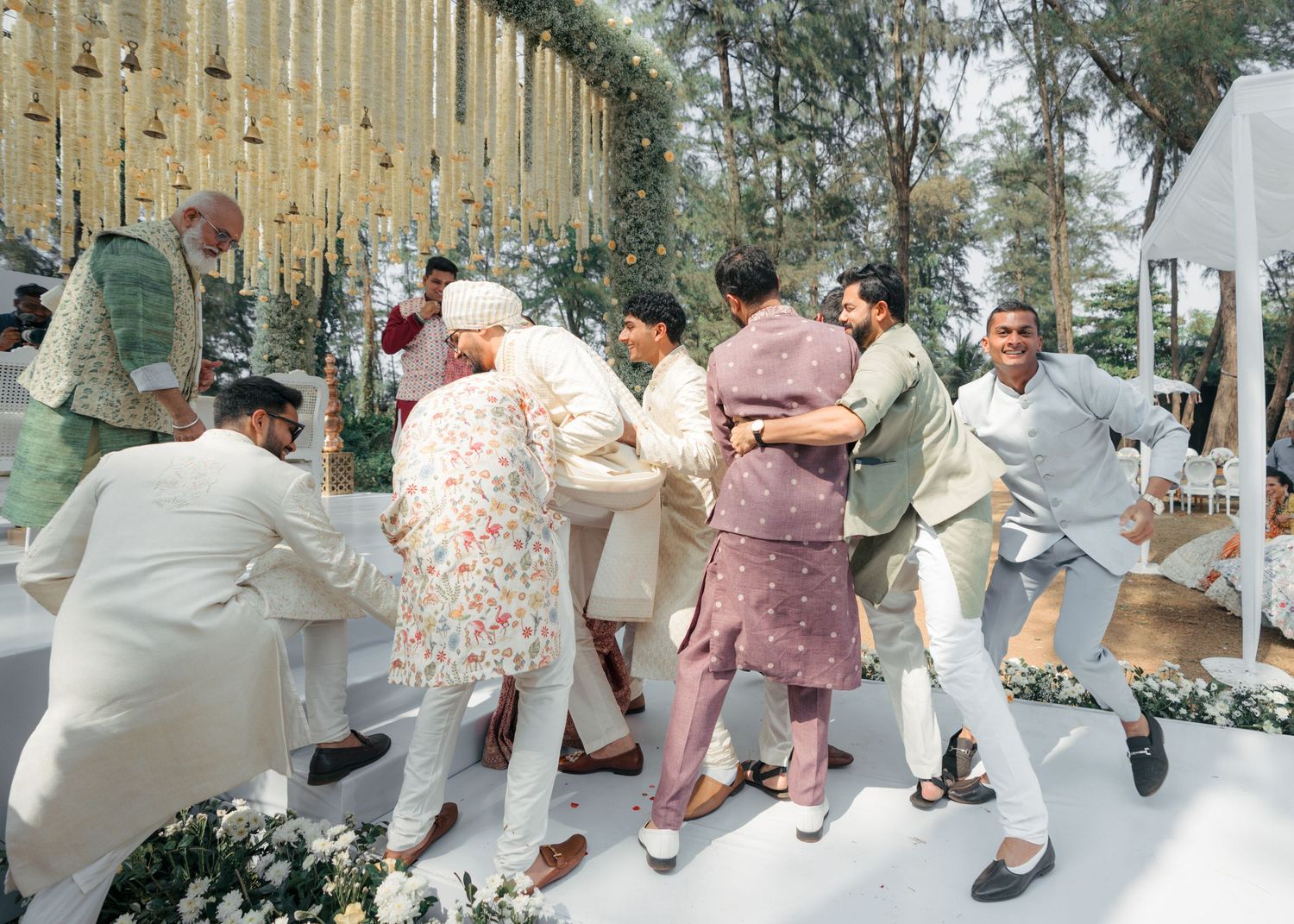 A group of people dancing in a conga line outdoors, dressed in casual 1950s style clothing.