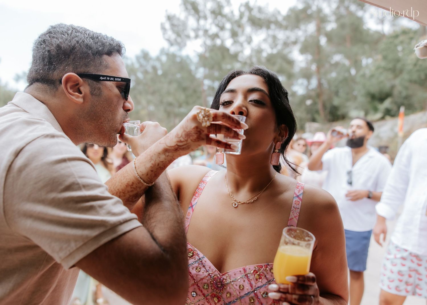 Two people taking shots at an outdoor party, woman holding orange juice, festive summer gathering.
