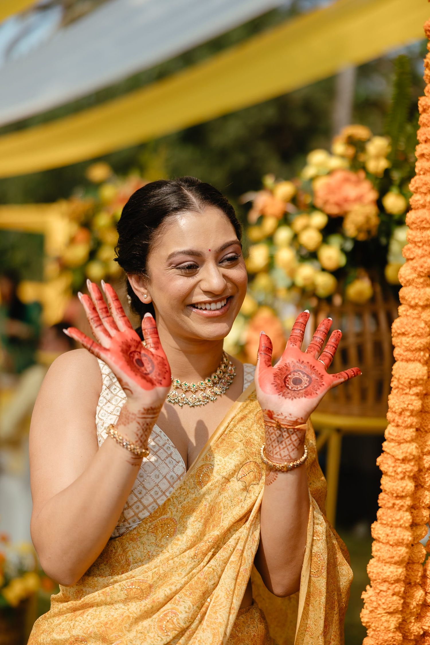 Smiling Indian bride in golden saree showing henna mehndi hands at traditional wedding ceremony.
