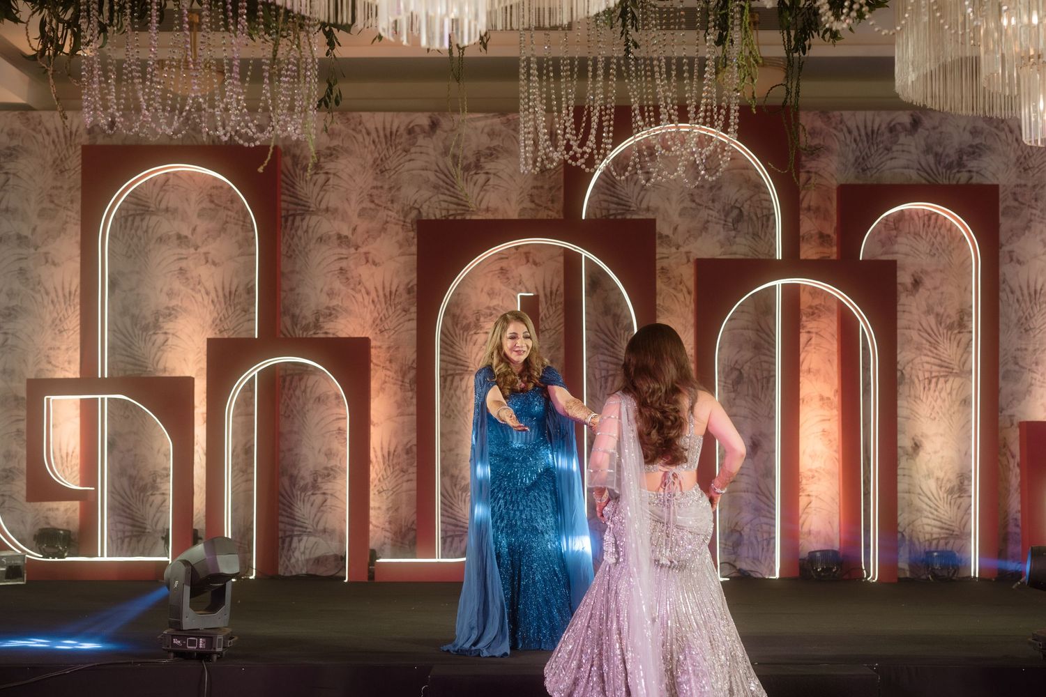 Two people in elegant gowns stand before illuminated archways in a dreamy, romantic setting.
