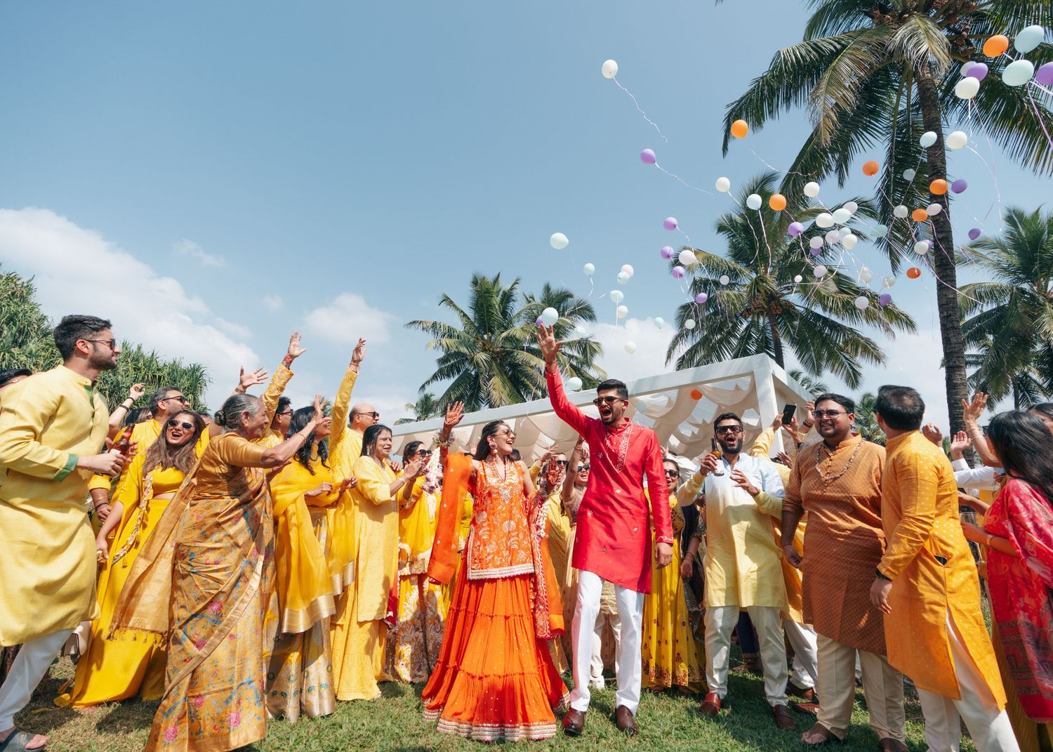 A group celebrating a festive occasion outdoors wearing vibrant yellow, orange and red traditional attire.