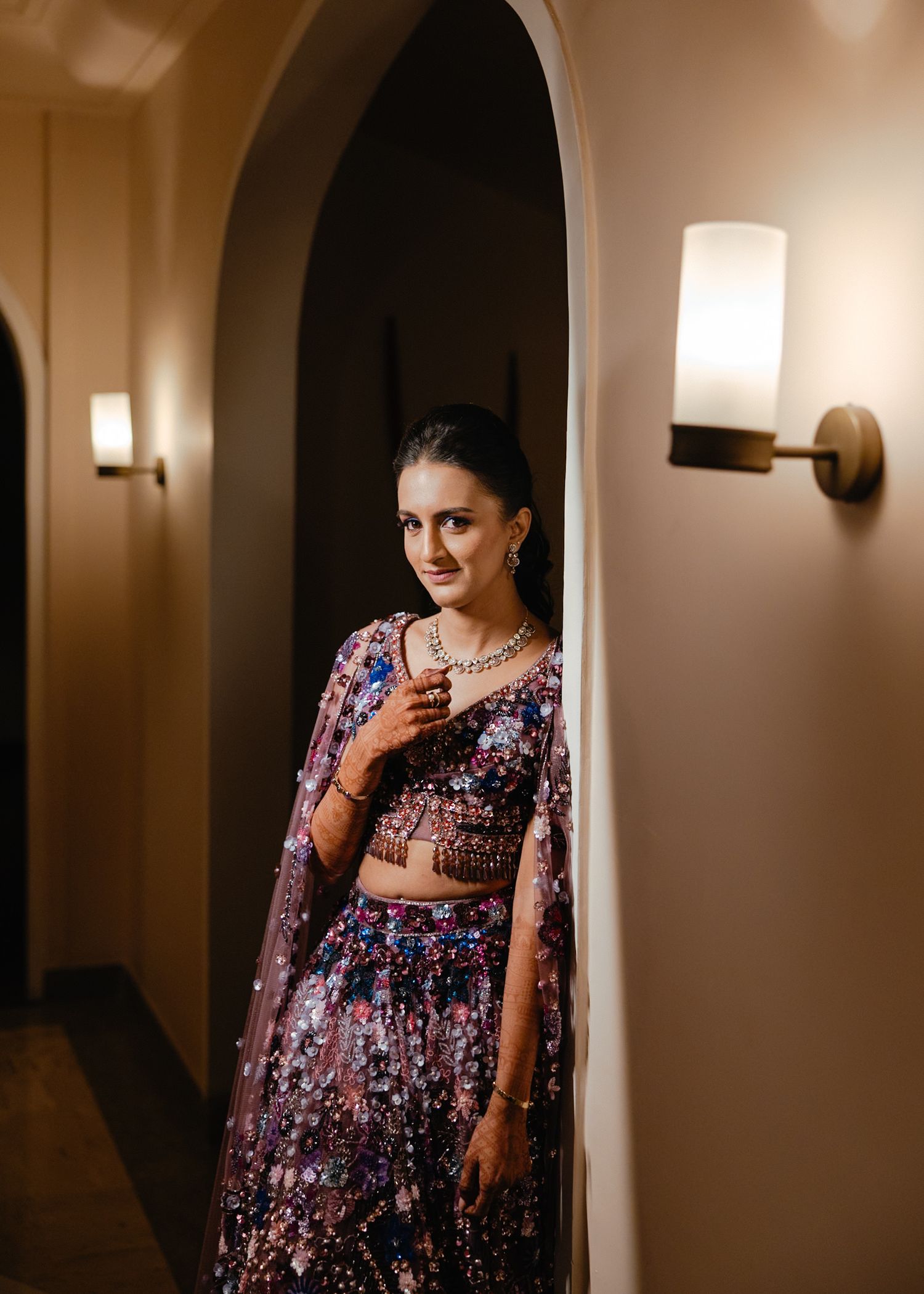 A person wearing a floral print dress poses in a dimly lit hallway with wall sconces.