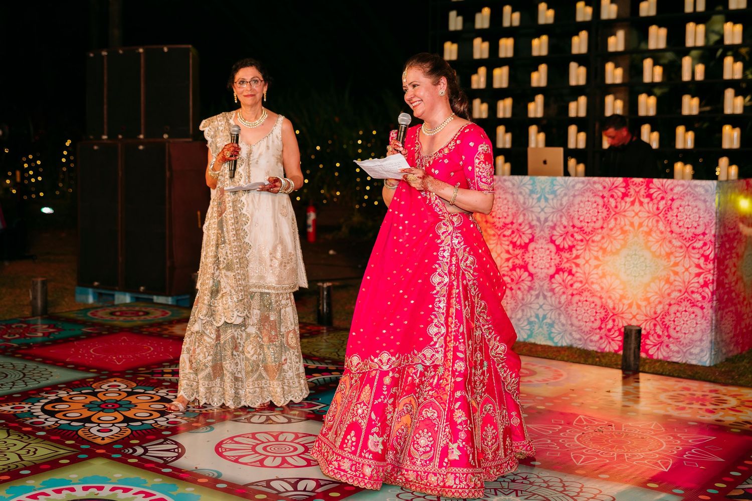 Two people perform a traditional dance performance in vibrant pink and gold cultural attire on an illuminated stage.