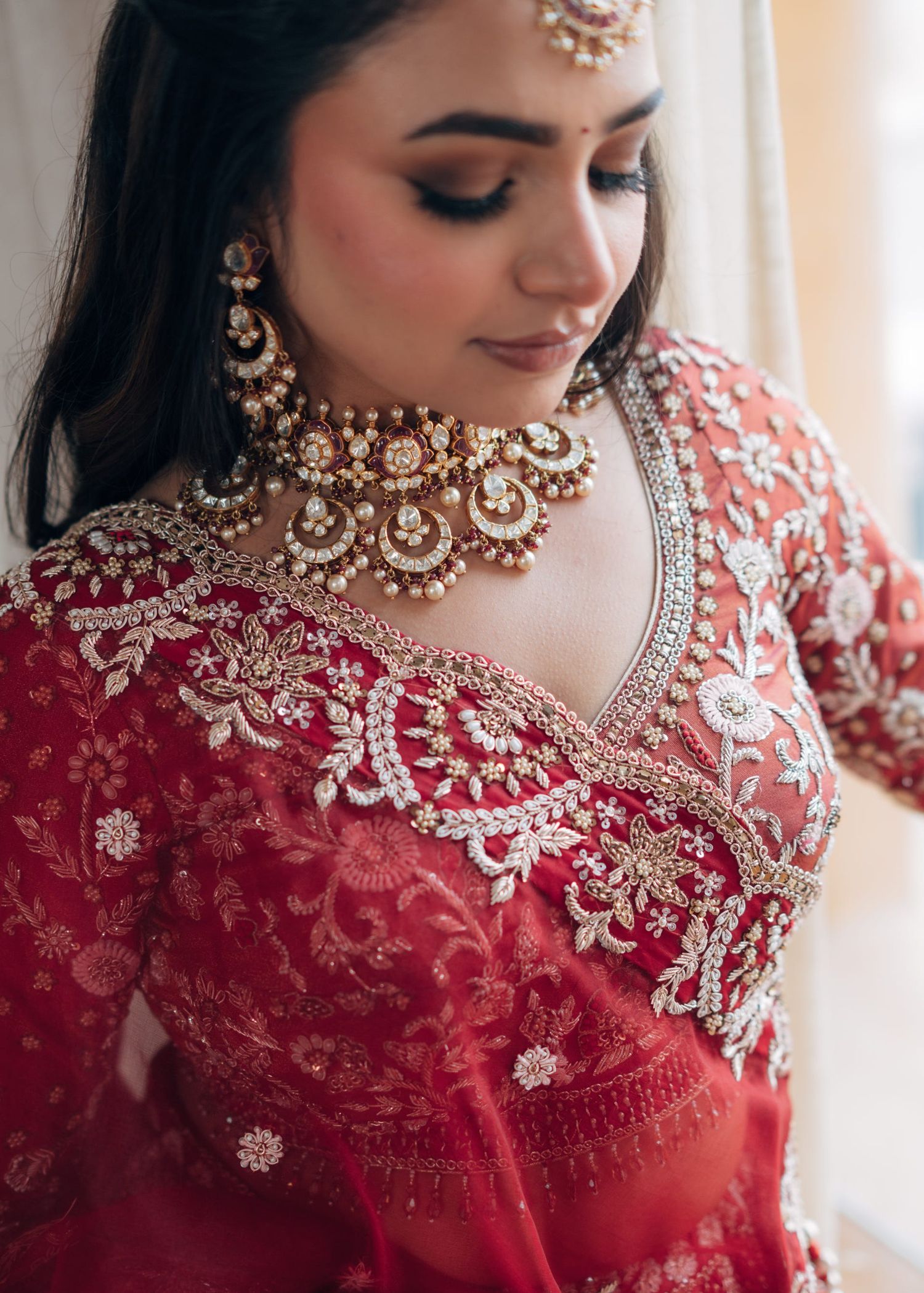 A South Asian bride in a red embroidered lehenga adorned with intricate silver and gold embellishments and traditional kundan jewelry.
