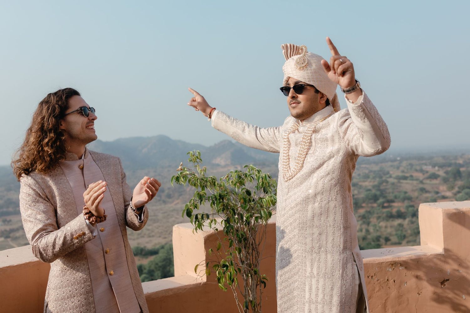 Groom and friends in white traditional outfits enjoying candid moments outdoors.