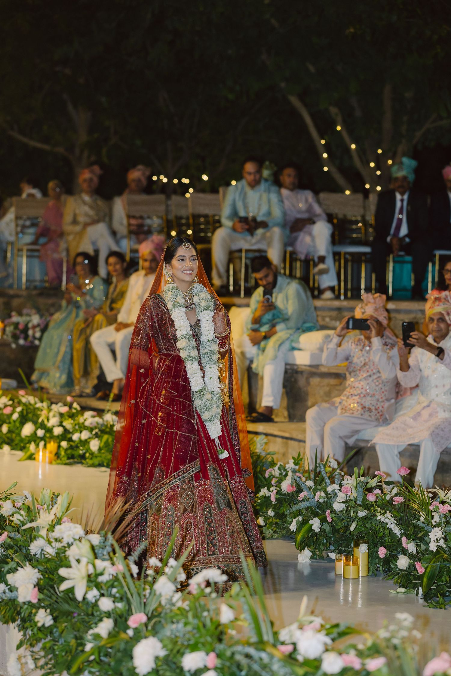 Outdoor evening wedding ceremony setup with white floral arrangements and traditional Indian decor.