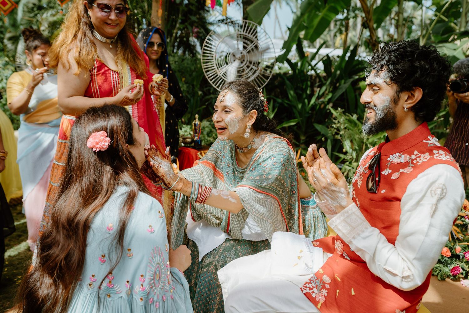 Joyful Indian wedding haldi ceremony with guests in colorful traditional attire outdoors.