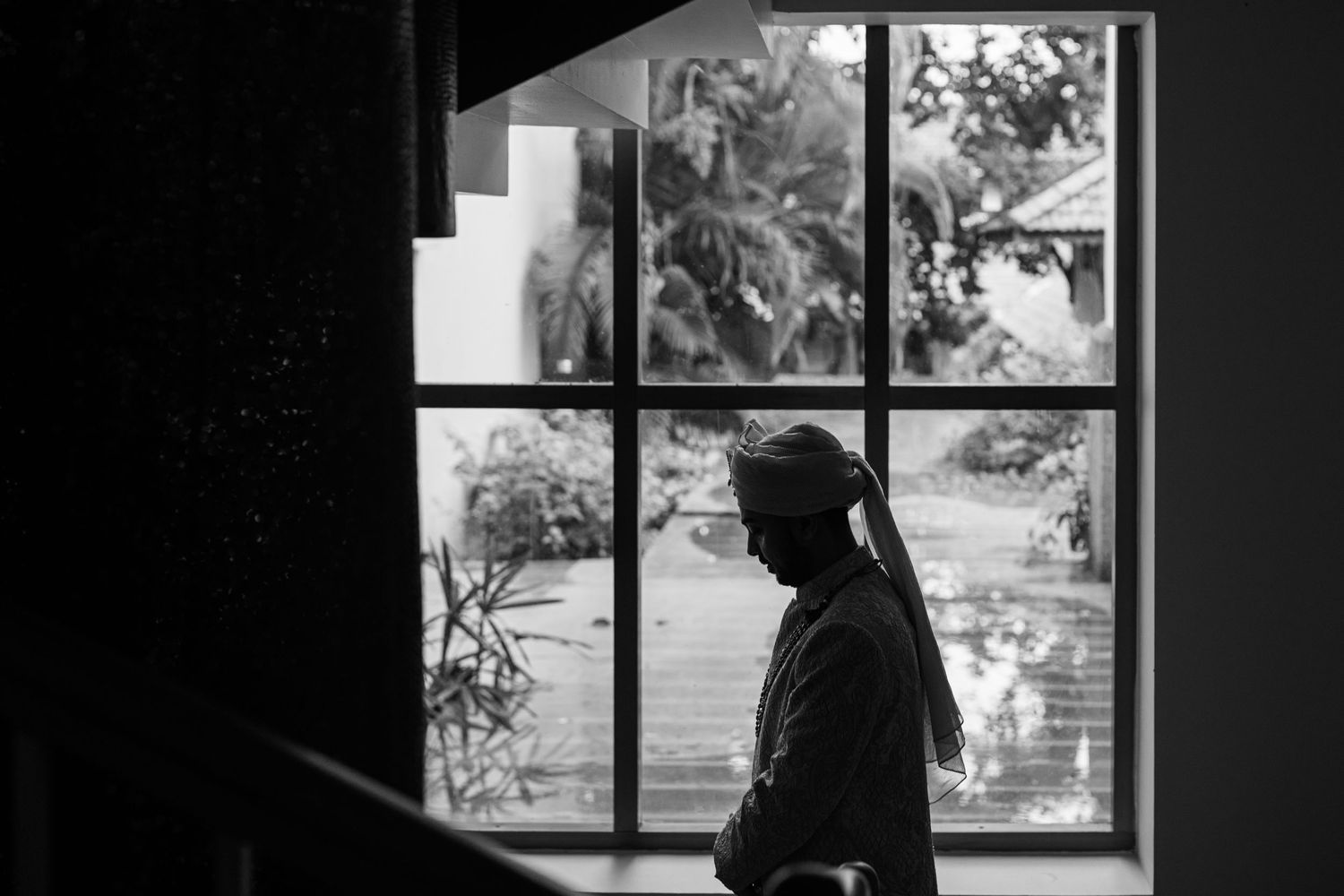Black and white silhouette of a pregnant woman standing by a large window with lush greenery outside.