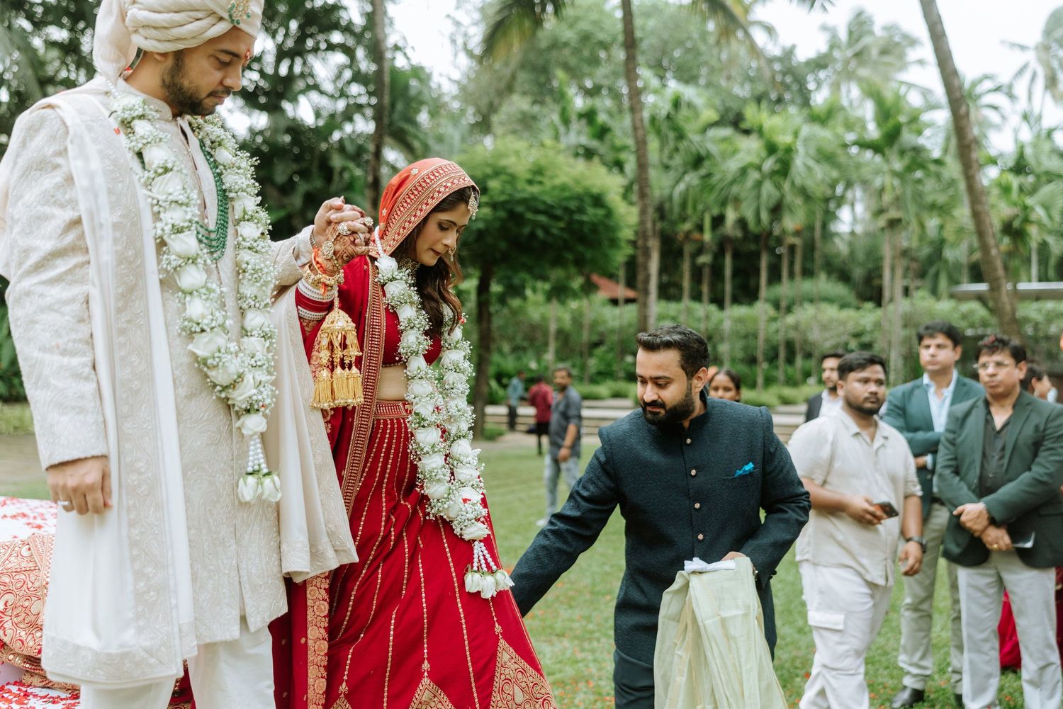 Indian bride in red lehenga and groom in white sherwani during traditional Hindu wedding ceremony outdoors.