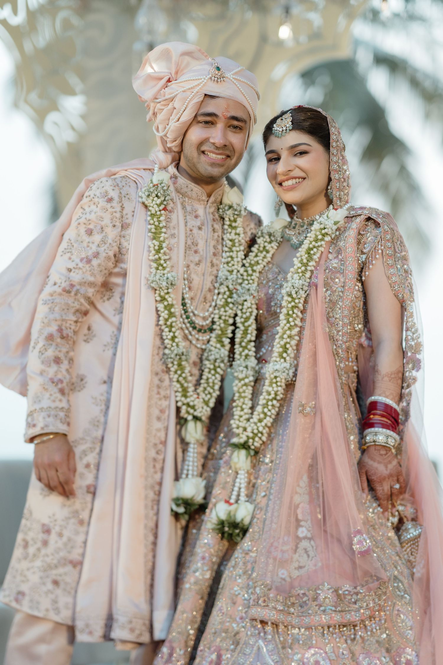 Joyful moments captured of a couple in traditional Indian wedding attire with floral garlands and pink outfits.