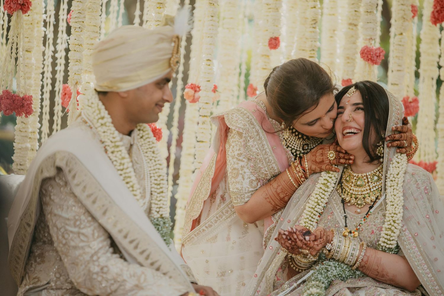 A traditional Indian wedding ceremony with participants wearing white and gold attire amid floral decorations.