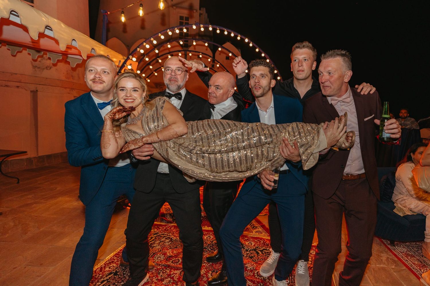 Evening wedding celebration with guests carrying someone in a festive moment.