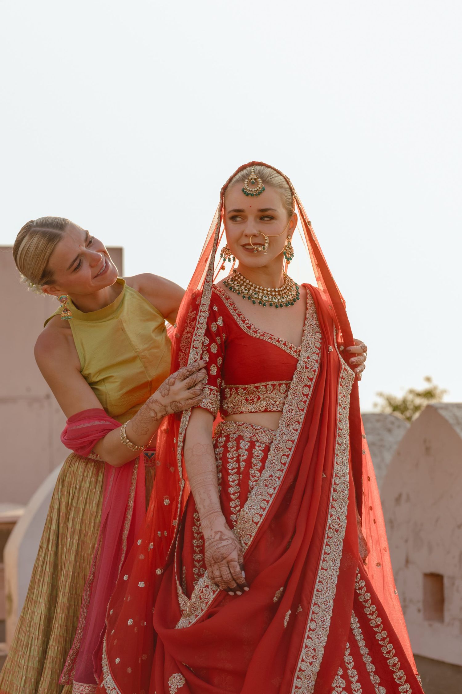 Traditional Indian bridal preparation with attendant adjusting red lehenga.
