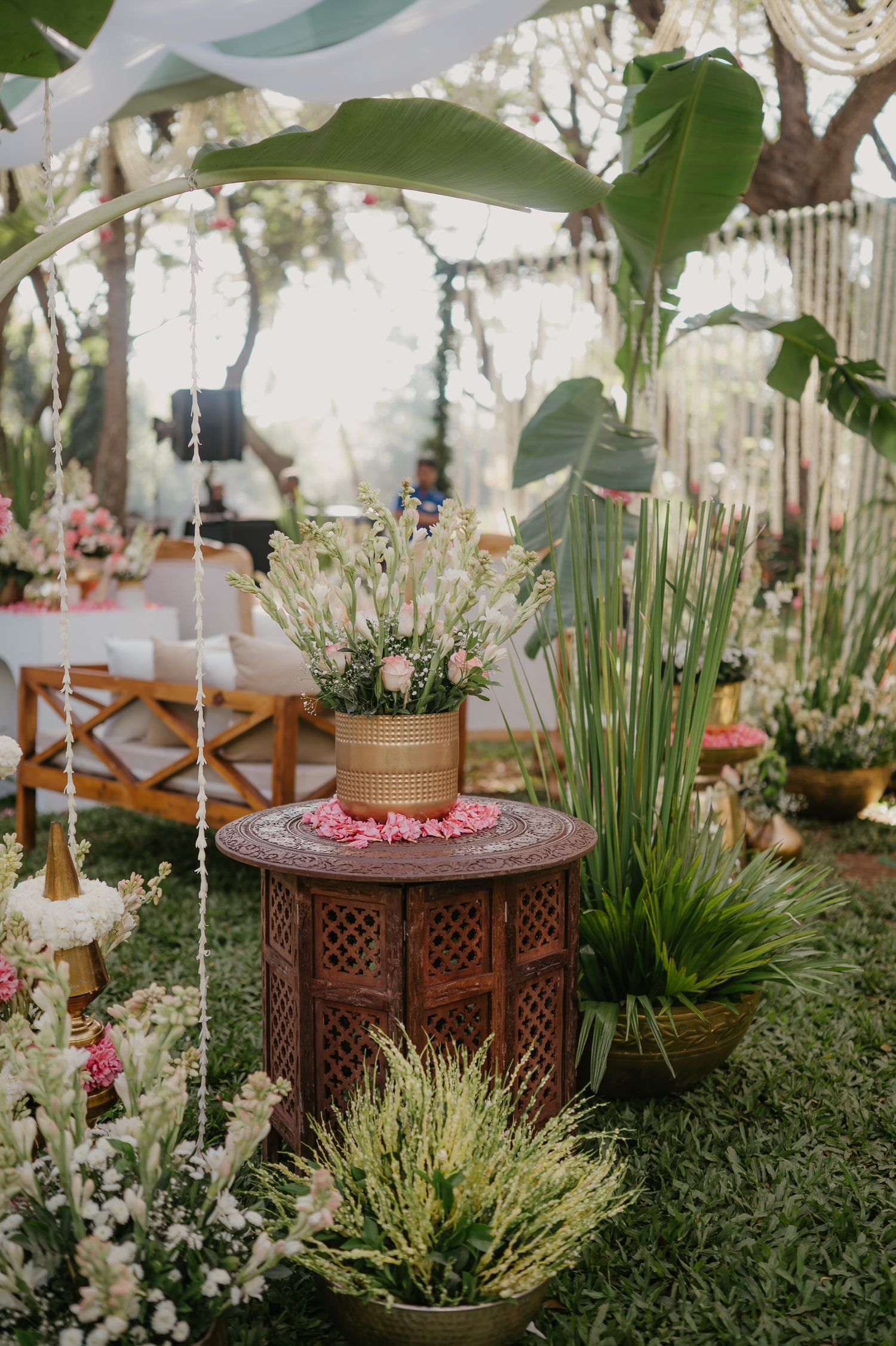 Elegant wedding reception decor features ornate wooden lanterns surrounded by lush greenery and pastel floral arrangements.