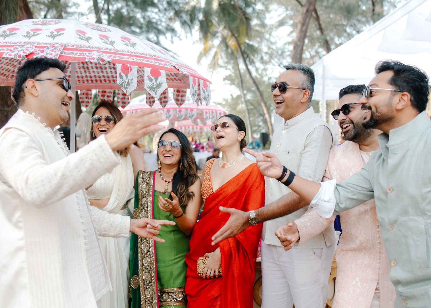 People in white and red attire dancing together at an outdoor celebration with palm trees in the background.
