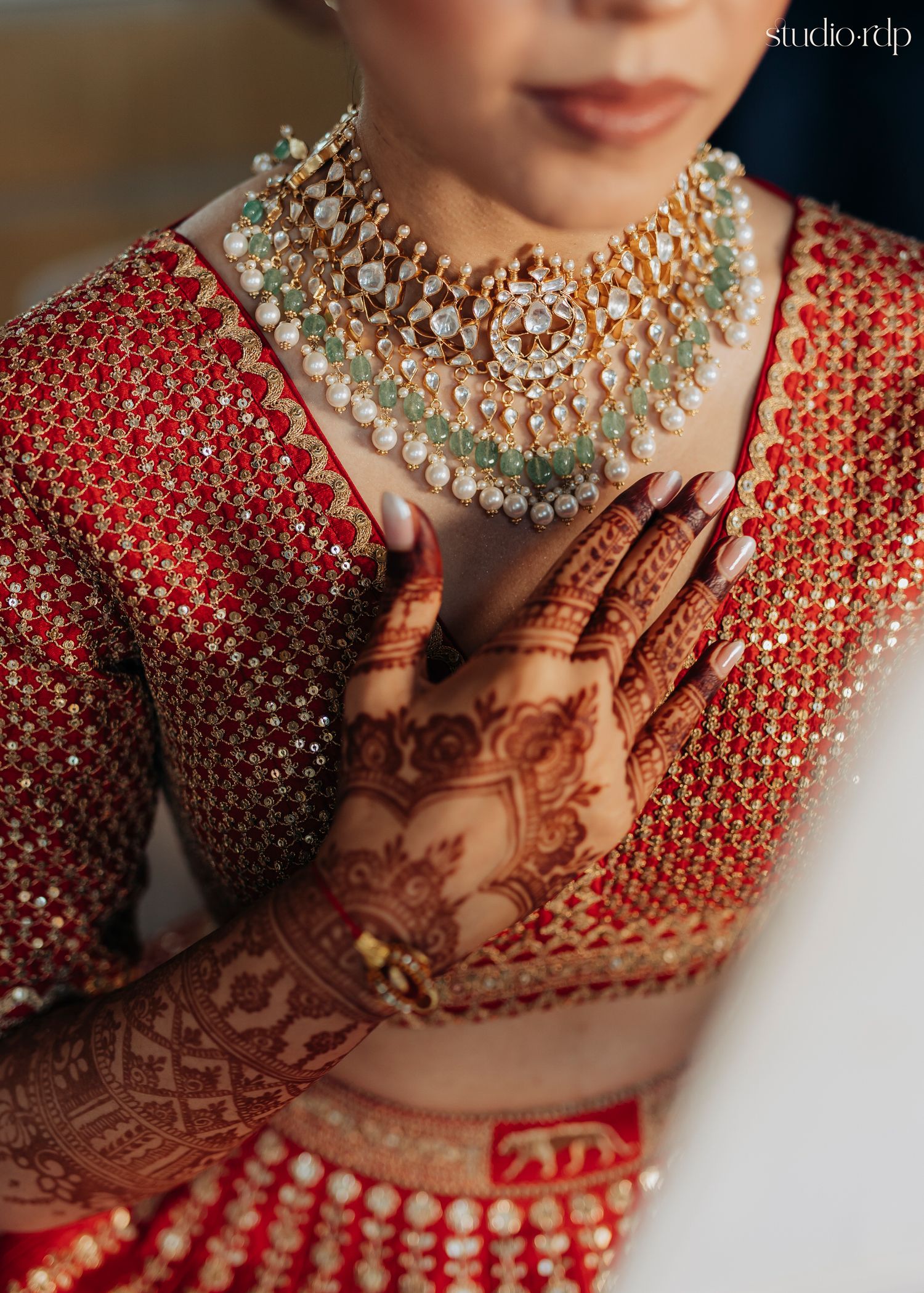 Traditional Indian bridal ensemble featuring intricate henna designs and ornate pearl necklace against red embellished attire.