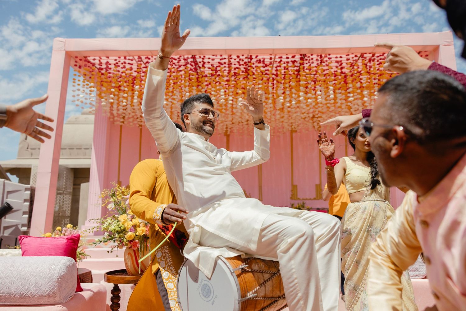 Joyful celebration at an outdoor wedding ceremony with pink decor and floral arrangements against a blue sky.