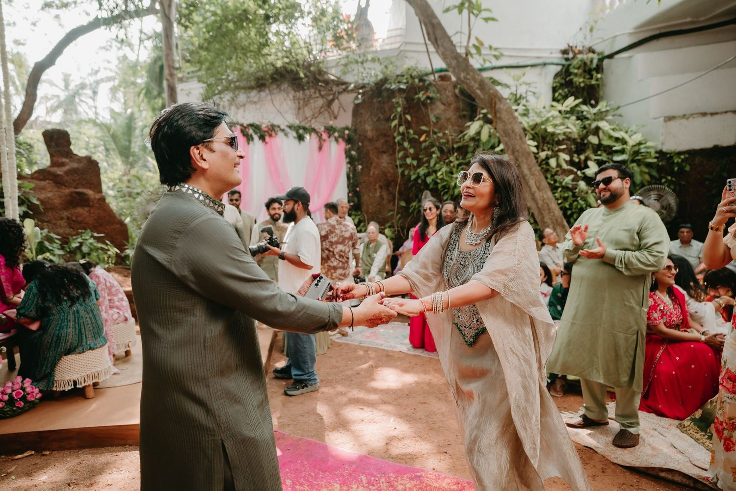 Couple dancing joyfully at a vibrant Indian wedding celebration outdoors, surrounded by guests in colorful traditional attire.