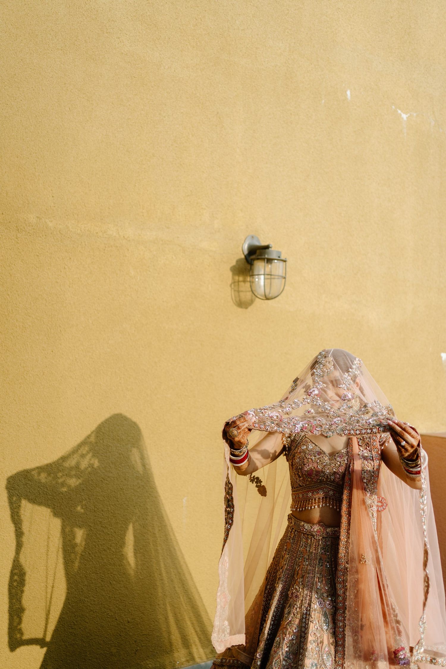Elegant bridal or formal dresses displayed in a row against a beige wall with dramatic shadows cast.