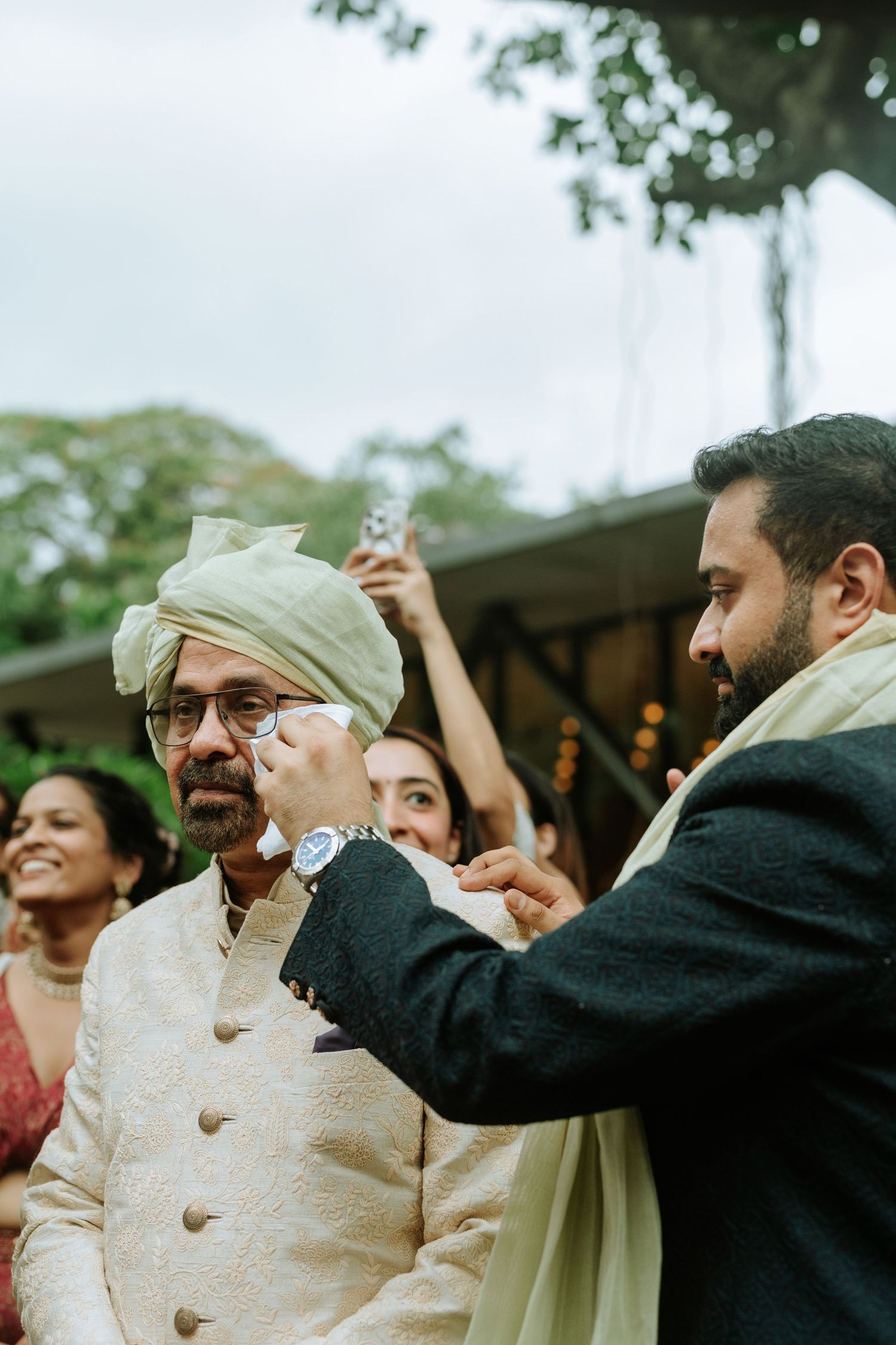 A man in traditional Indian attire receives a heartfelt gesture at a wedding ceremony outdoors.