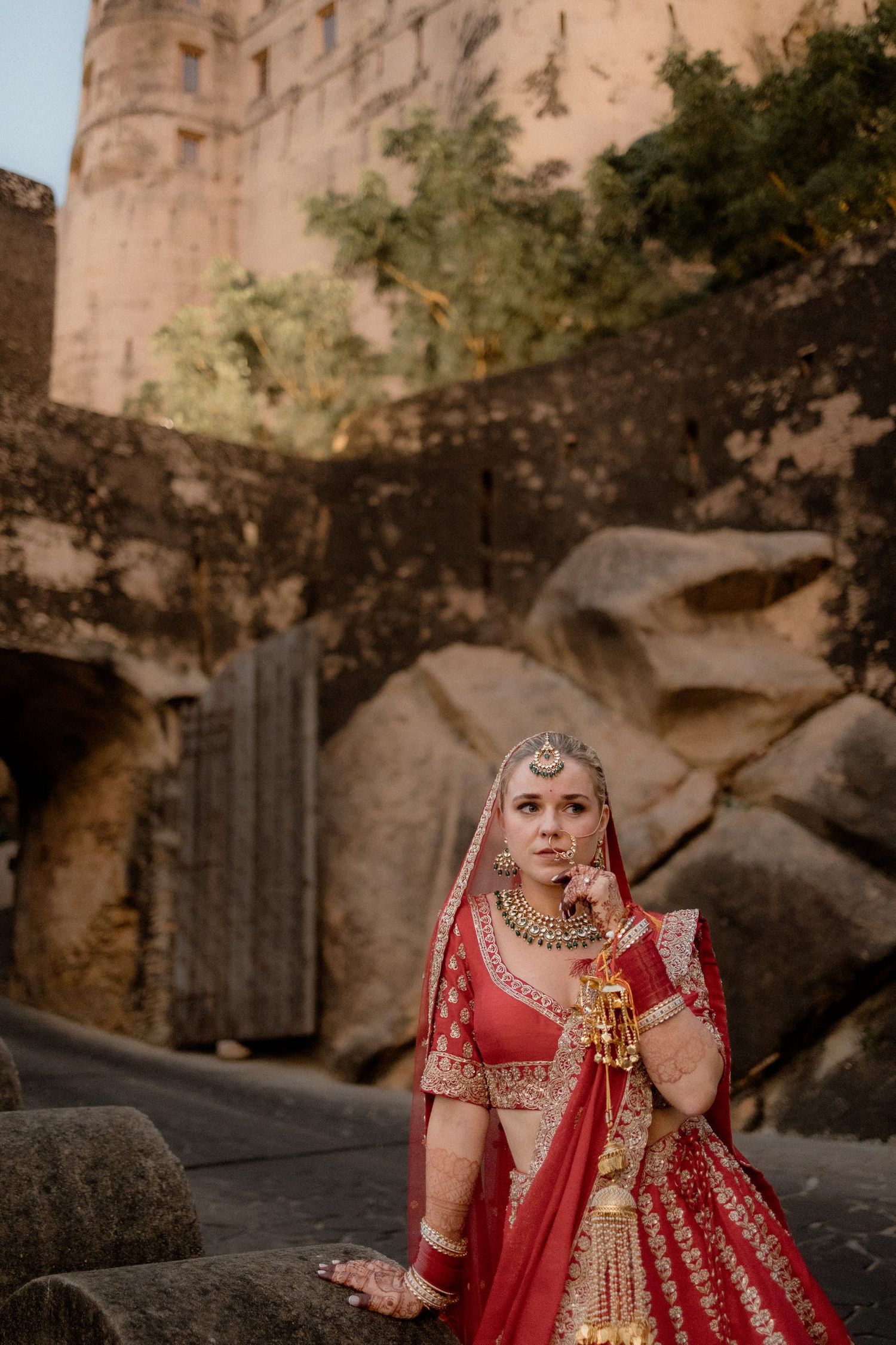 Traditional Indian bridal attire photographed against stone fortress walls at sunset.