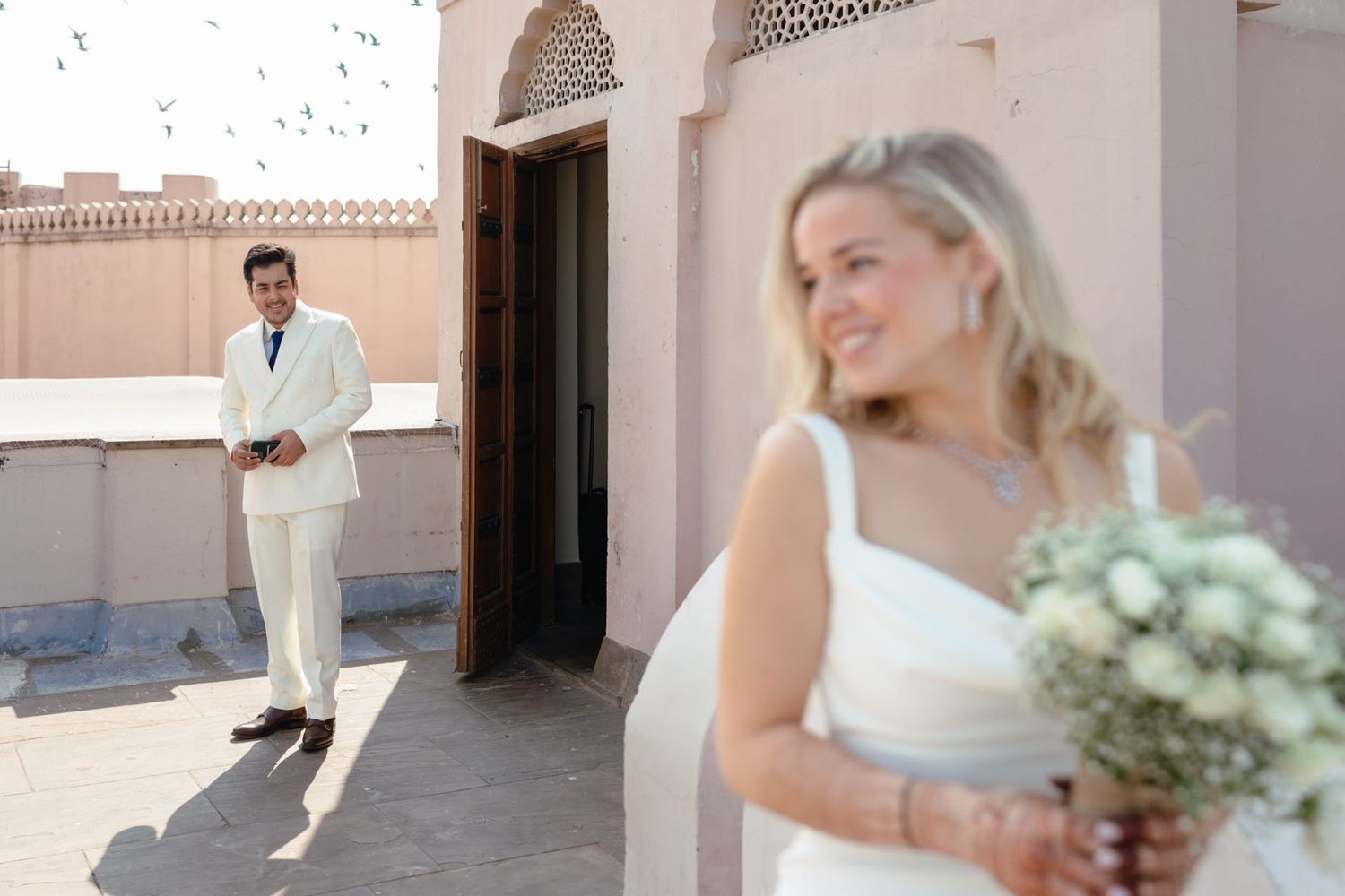 Wedding couple in cream and white attire pose separately against desert architecture.