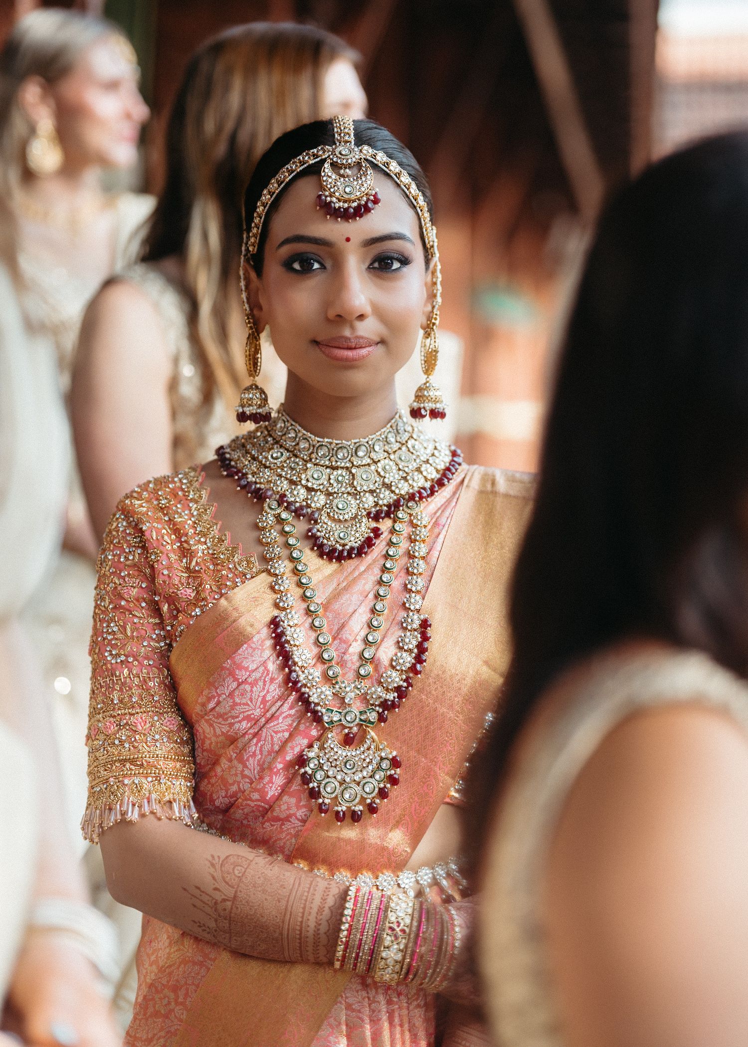Traditional Indian bridal portrait showcasing elaborate jewelry and coral-colored attire.