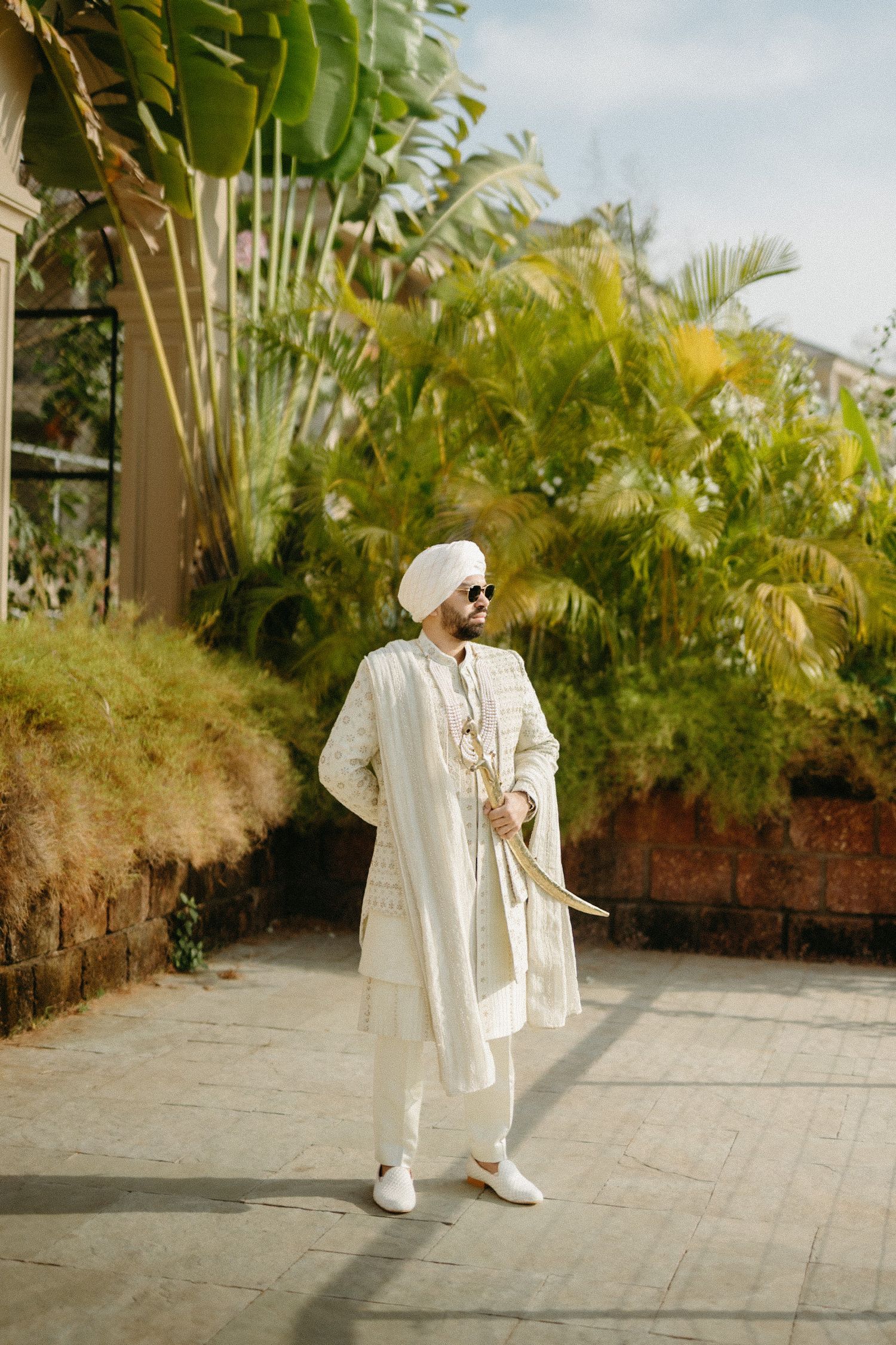 Person in a flowing white traditional outfit strikes stylish poses against a palm tree backdrop on a sunny day.