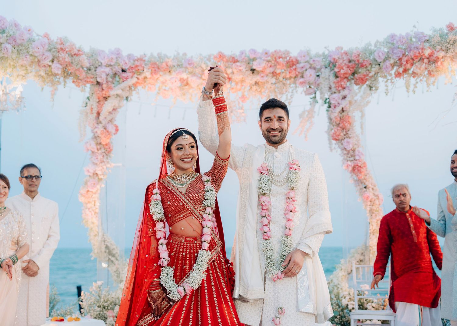 Wedding ceremony setup on a beach with white decor and pink floral arrangements along the aisle and arch.