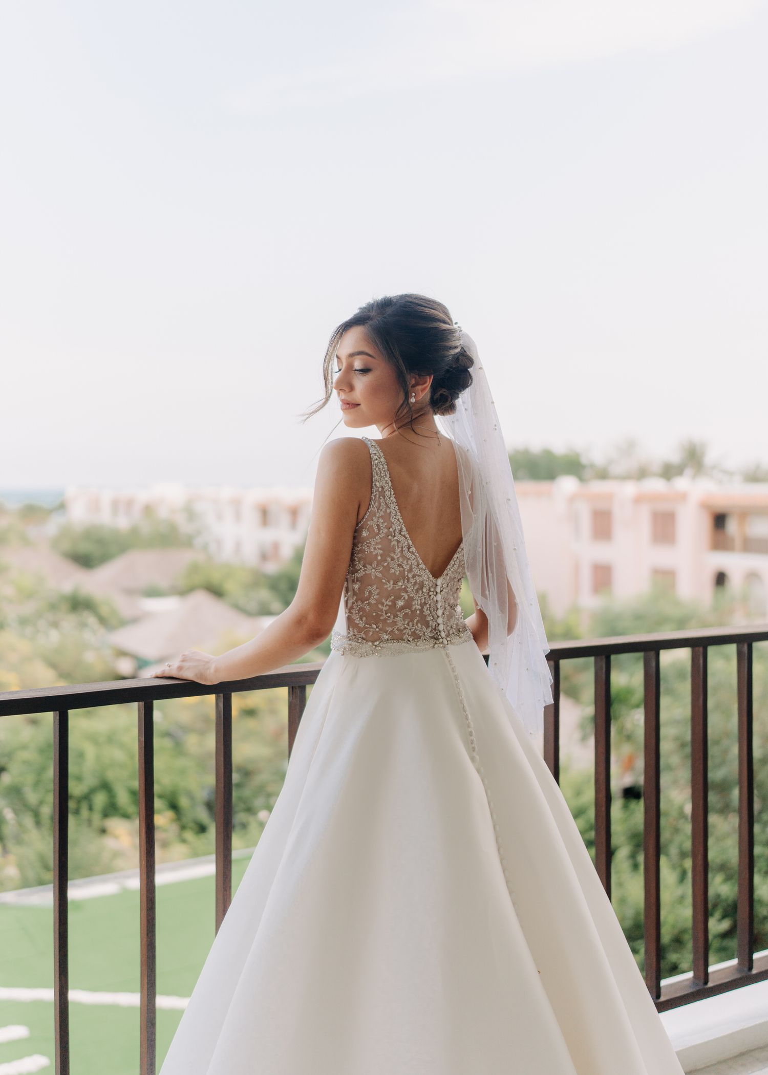 Bride in a white ballgown wedding dress stands on a balcony overlooking a golf course on her wedding day.