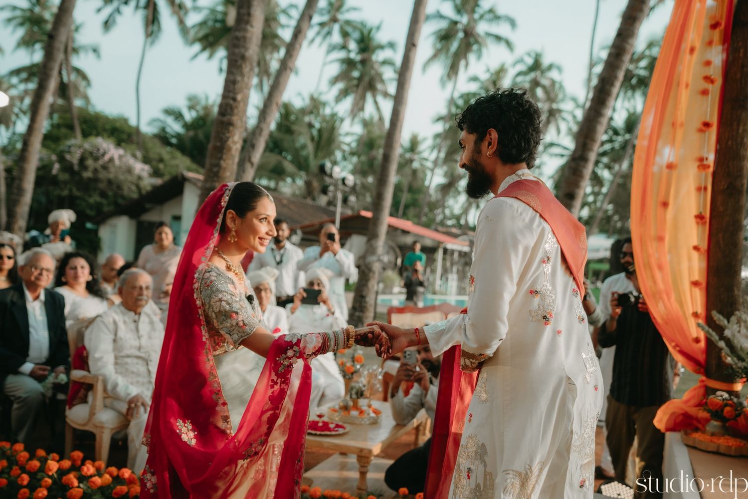 Outdoor wedding ceremony with orange and red decor surrounded by tropical palm trees.