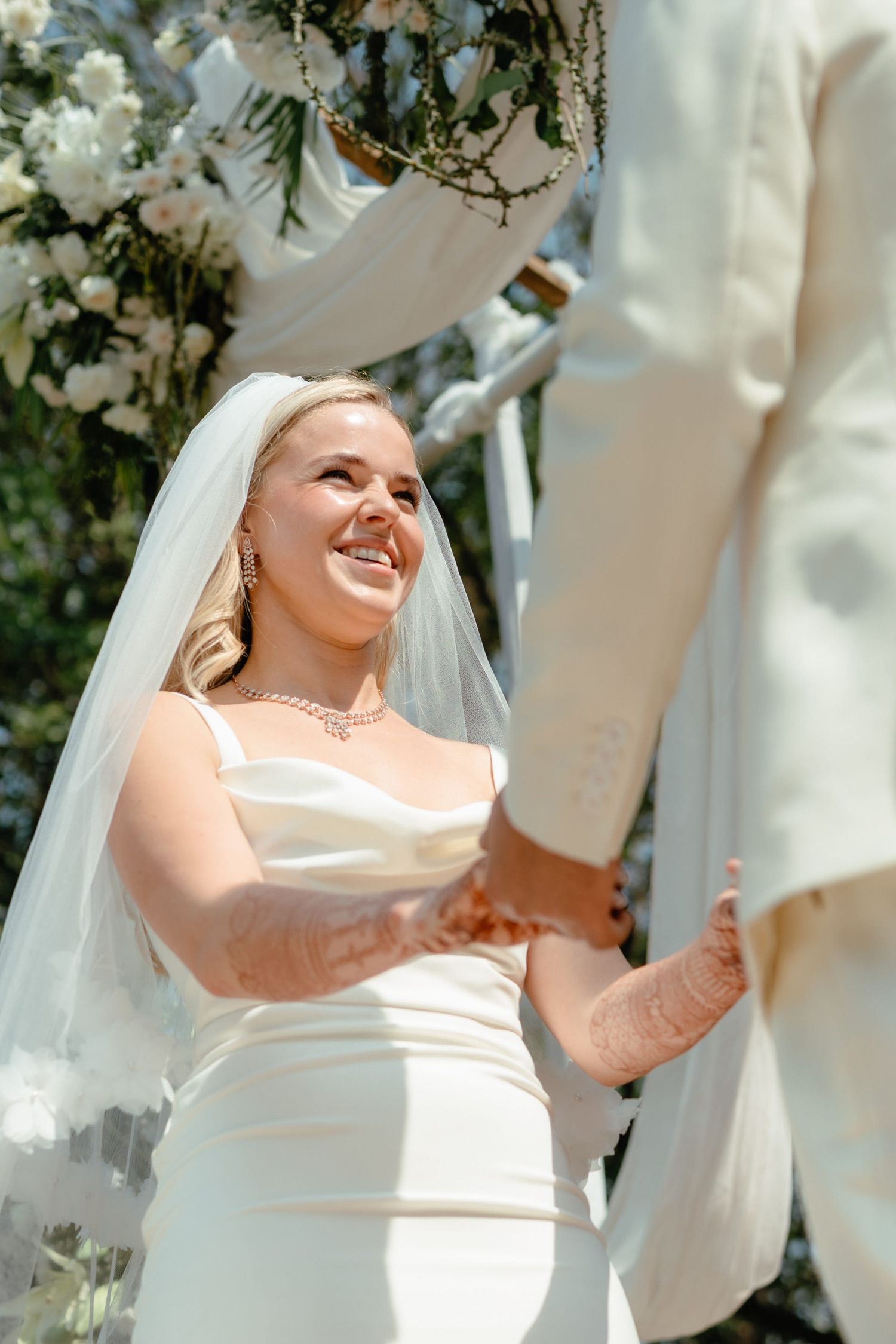 A joyful moment captured during an outdoor wedding ceremony under a white floral arch.