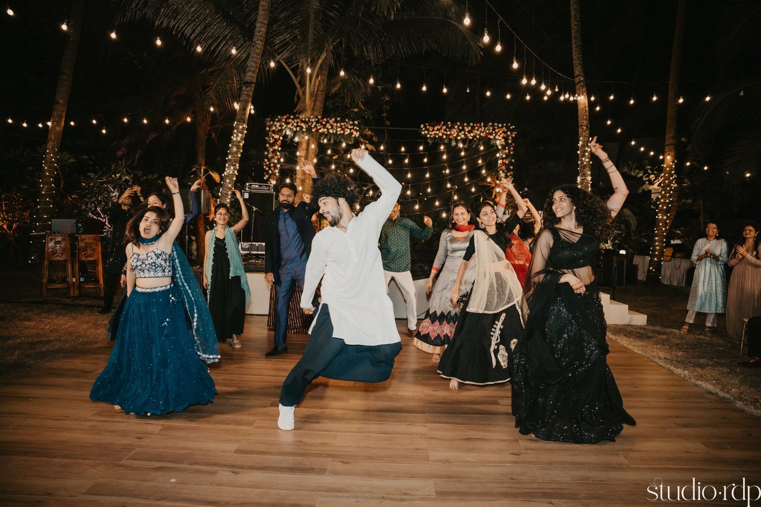 Celebration attendees dance with raised arms under string lights at an outdoor evening event.