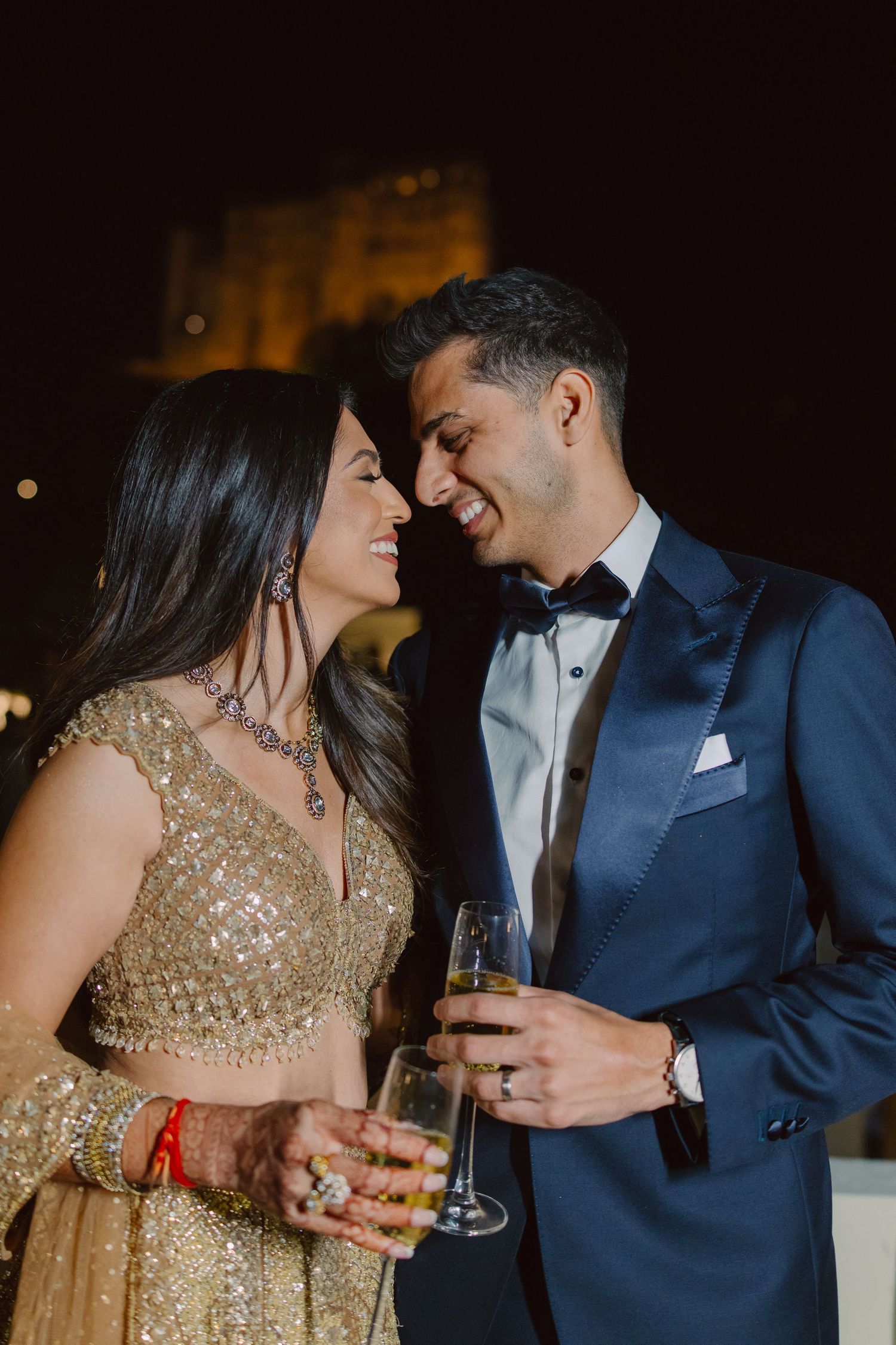 Romantic couple sharing intimate moment while holding champagne glasses at evening celebration.