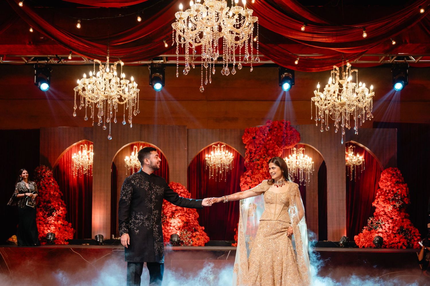 Bride and groom share a romantic first dance under crystal chandeliers at an elegant red-themed Indian wedding reception.