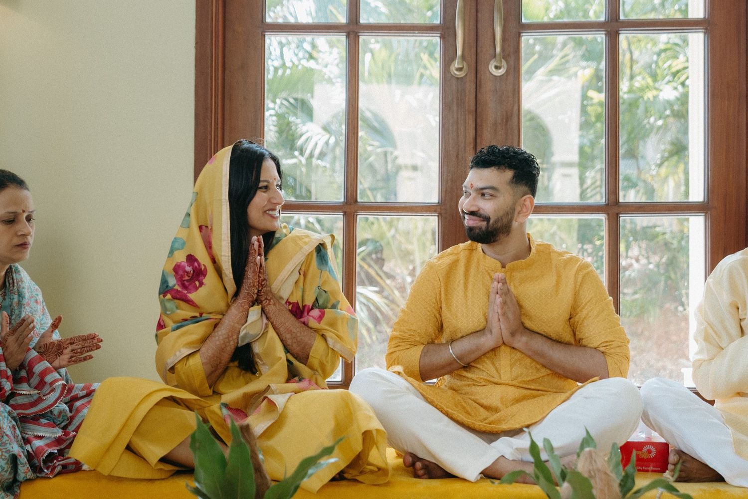 People in yellow traditional attire sit together beside a window and share a meal.