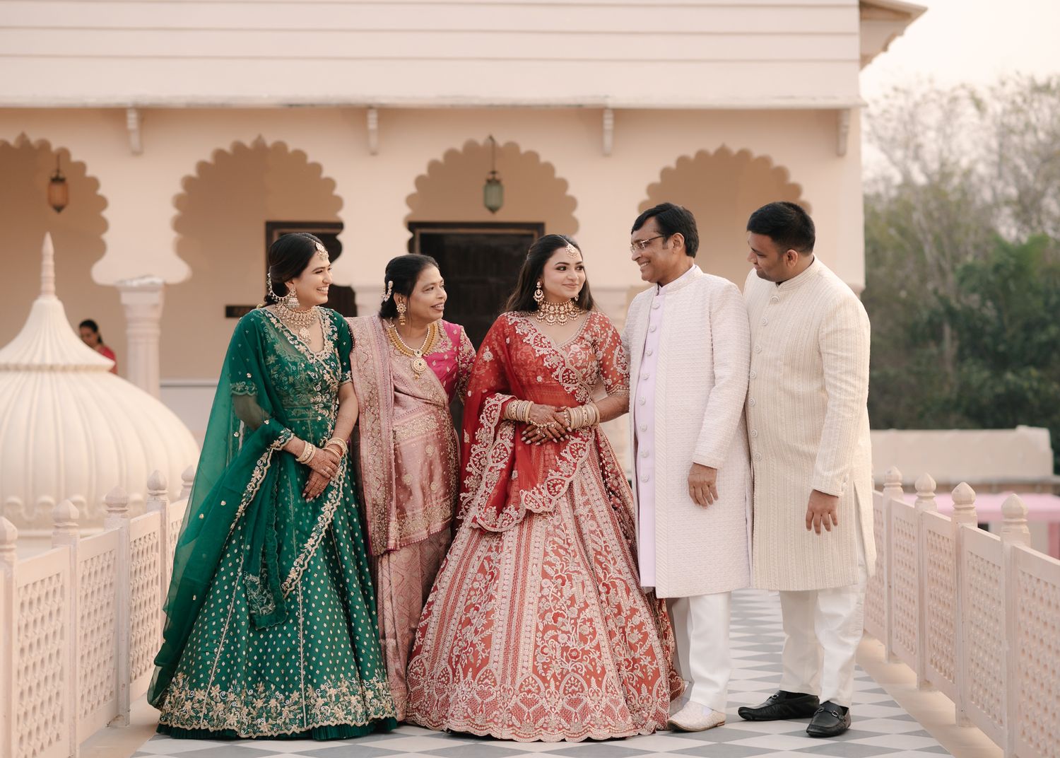 Indian bride in red lehenga posing with family members in green and white ethnic outfits.