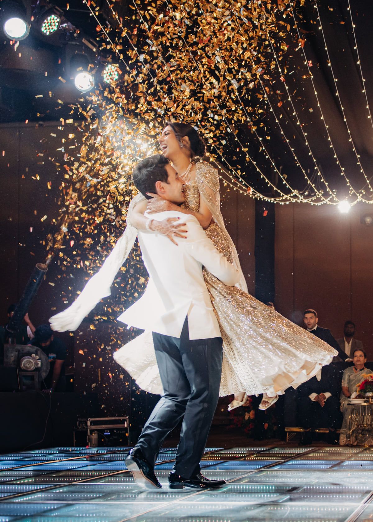A romantic dance under twinkling golden lights with confetti falling during a wedding celebration.
