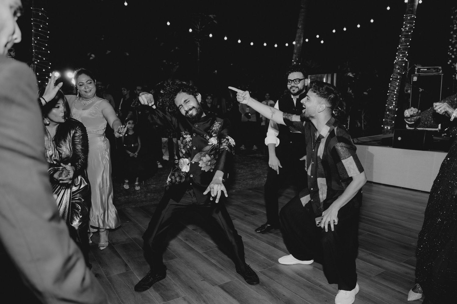 Black and white photo of guests dancing energetically at a wedding reception under string lights.
